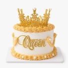 Gold crown cake with "Queen Birthday" topper, white frosting, and piped details.