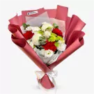 A bouquet of red, white, and green flowers wrapped in pink paper, tied with a white ribbon.