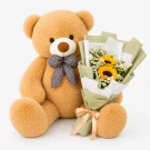 Giant light brown teddy bear with a blue checkered bow holding a bouquet of sunflowers and greenery.