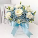 White roses, carnations, and blue baby's breath in a white box with a blue ribbon.