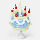 A blue and yellow balloon cake with white balloon accents, red cherries, green stems, and yellow candle balloons on a white stand.
