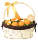 Woven basket filled with vibrant oranges, green leaves, and white flowers, adorned with a gold bow and "with love" tag.