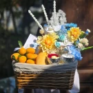 Wicker basket with artificial flowers, yellow fruit, and small silver bowls.