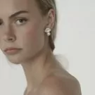 Model wearing pearl droplet earrings, close-up of face and shoulders.