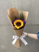 Sunflower bouquet with purple statice flowers, eucalyptus, and a white ribbon, wrapped in brown paper.