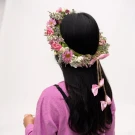 Woman with black hair wearing a large fresh flower crown with pink bows and greenery.