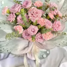 Bouquet of pink roses and carnations with eucalyptus leaves, wrapped in light green paper with butterfly designs.