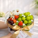Round clear bowl filled with green plums, strawberries, cherries, and a flower garland.