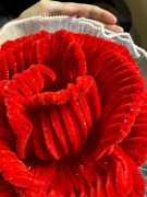 Close-up of a large, red velvet rose with glittery accents and a ruffled white trim.