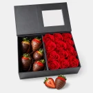 Chocolate-covered strawberries and red artificial roses arranged in a black gift box.