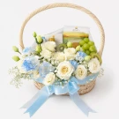 Floral gift basket with white roses, blue carnations, grapes, kiwi, and packaged food items.