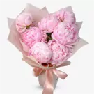 A bouquet of seven pink peonies with light pink paper wrapping and a satin ribbon.
