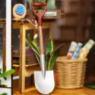Miniature shovel and snake plant in a DIY book nook kit on a wooden shelf.