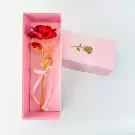 Red and gold artificial rose in a pink gift box with a bow.
