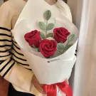 Crochet red rose bouquet with green leaves, wrapped in white paper and tied with a red ribbon.