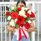 A round white box overflowing with red and white roses, tulips, gerbera, carnations, and eucalyptus, tied with a red and white ribbon.