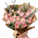 Bouquet of 24 pink roses, eucalyptus, and tiny white flowers wrapped in brown paper.