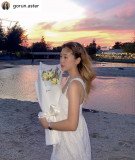 Woman in white dress holding white flowers by the water at sunset.