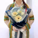 Graduation bouquet in a clear balloon with yellow gerberas and white roses, topped with a mini graduation cap.