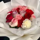 A bouquet of pink, red, and white roses and carnations wrapped in white paper.