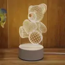 Acrylic teddy bear lamp with heart, illuminating a warm light on a wooden surface.