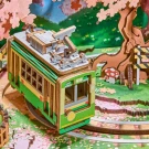 Green tram model on wooden tracks with cherry blossoms, a tree, and a mushroom.