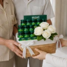 An elderly woman holds a bottle of Brand's Essence of Chicken next to a hamper filled with bottles and white flowers.