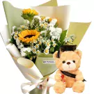 Graduation teddy bear with black cap and diploma beside a bouquet of sunflowers and daisies.