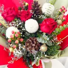 A festive bouquet with red roses, white ping pong flowers, pine cones, berries, and Christmas ornaments.
