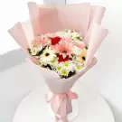 A pink bouquet of gerberas and white daisies with red carnations, wrapped in pink paper and tied with a pink ribbon.