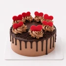 Chocolate cake with chocolate frosting, chocolate drips, chocolate sprinkles, and red heart decorations.