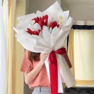 Crocheted red and white tulips bouquet with red ribbon, held by a person.