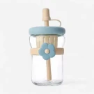 Clear glass water bottle with blue lid, beige flower accent, and straw.
