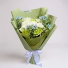 White and green flowers with blue accents, wrapped in light green paper and tied with a white ribbon.