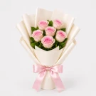 Pink roses arranged in a bouquet, wrapped in white paper and tied with a pink ribbon.