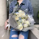 White roses and blue hydrangeas arranged in a bouquet with sheer wrapping, held by a person in ripped jeans.