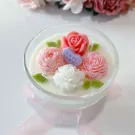 Glass candle with pink and white sculpted flowers, green leaves, and a purple "love you" candy.