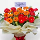 Bright gerbera daisies in red and orange arranged in a bouquet with a "Congratulations" card.