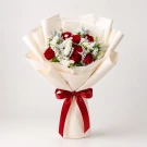 A bouquet of red roses, white statice, and dusty miller wrapped in cream paper and tied with a red ribbon.