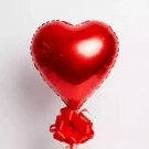 Red heart-shaped foil balloon tied with a red bow against a white background.