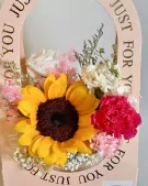Graduation Bloom Basket: Sunflower, roses, carnations, and baby's breath in a pink arch box with "Just for You" text.