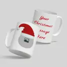 Two white mugs with a Christmas theme. One mug has "Your Christmas message here" in red text, the other has a Christmas hat and a placeholder image.