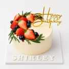 White frosted red velvet cake with strawberries, blueberries, rosemary, and "Happy Birthday" topper.