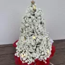 White gypsophila Christmas tree with fairy lights and star topper, on a red base.