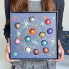 A person holds a galaxy-themed chocolate box with 12 planet-shaped chocolates inside.