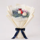 Graduation bouquet with two white bunnies wearing graduation caps, surrounded by small blue flowers and wrapped in cream paper.