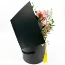 Black graduation hat-shaped box filled with pink money roses, white mums, and eucalyptus.