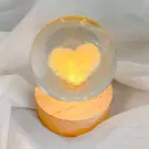 Crystal ball with glowing yellow heart on wooden base.
