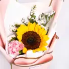 Sunflower bouquet with pink carnations and baby's breath, wrapped in pink and white paper.