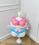 Bubblegum pink and blue balloon cake with a candle and cherries, on a white pedestal.